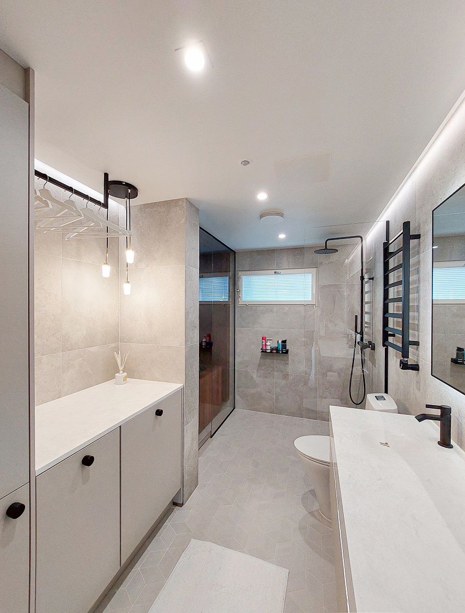 A bathroom with a light surface illuminated by downlights and a led strip mounted on the ceiling and on the long sides of the ceiling. Additional pendant light.